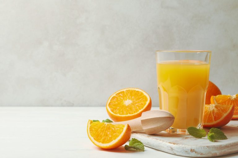 Frutas Adamo es tu proveedor de confianza en la Costa del Sol. Tablero con vaso de zumo de naranjas y naranjas sobre fondo de madera.